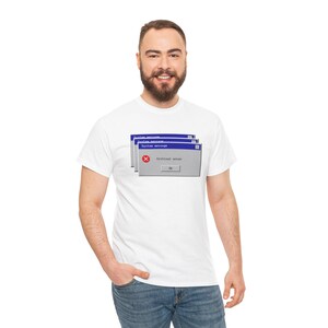 Può includere: T-shirt bianca con una grafica di un messaggio di errore del computer. Il messaggio di errore è visualizzato in una finestra blu e grigia con il testo "Critical error" e un simbolo "X". La maglietta è realizzata in un materiale morbido.