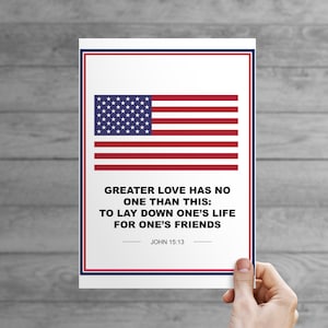 May include: A white card with a blue and red American flag at the top and a quote from the Bible, John 15:13, in black text. The quote reads: "Greater love has no one than this: to lay down one's life for one's friends."