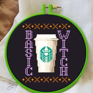 May include: A black and white embroidery hoop with a green and white coffee cup design. The text "BASIC WITCH" is embroidered in purple on the hoop.