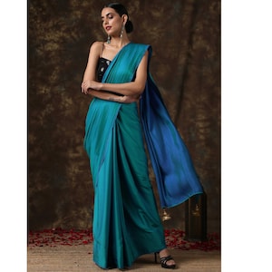 May include: A woman wearing a teal blue and dark blue saree with a black sleeveless blouse. The saree has a thin blue border.
