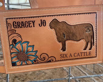 Puede incluir: Una manta de silla de montar de cuero marrón con un diseño de girasol, una silueta de vaca y el texto "GRACEY JO SIX A CATTLE".
