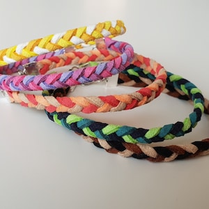 Könnte beinhalten: Fünf geflochtene Stoffarmbänder in verschiedenen Farben, darunter Gelb, Rosa, Orange, Grün und Braun.