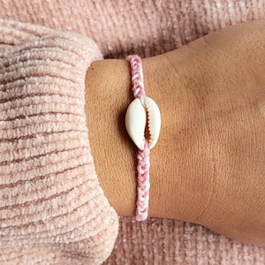 Peut inclure: Un bracelet tressé rose et blanc avec un charme de coquillage blanc.