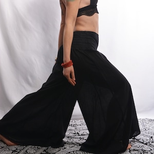 May include: A woman with red hair wearing a black bra with lace trim and black wide-leg pants. She has a tattoo on her upper arm.