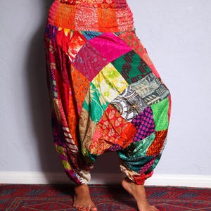 May include: Multicoloured patchwork trousers with a high waist and a loose, flowing fit. The trousers are made from a variety of fabrics in different colours and patterns, including red, pink, green, blue, and yellow.