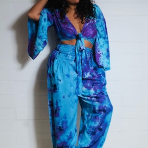Op de afbeelding: Een blauw en paars tie-dye crop top en bijpassende broek. De top heeft een strik aan de voorkant en de broek heeft een elastische tailleband.
