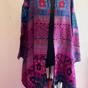 Peut inclure: Un châle à motifs dans les tons de bleu, rouge et violet, présenté sur un mannequin. Le châle présente un motif floral et géométrique répétitif avec des franges sur le bord inférieur. La palette de couleurs comprend des bleus profonds, des rouges vifs et des violets riches.