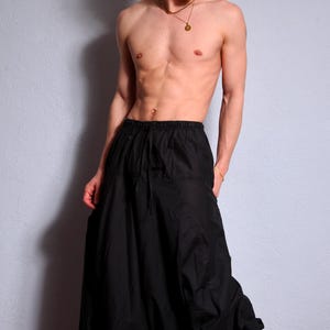 May include: A person wearing black harem pants with a drawstring waist. The pants are loose fitting and flowy.