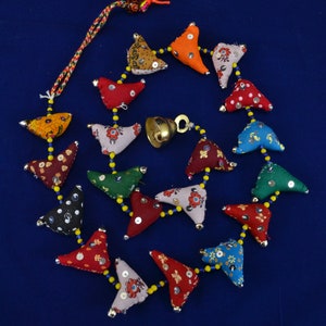 May include: A vibrant garland composed of fabric triangles in diverse patterns and hues, such as red, orange, and blue, connected by yellow beads. A small brass bell is suspended in the middle, and a multicoloured tassel decorates the top.