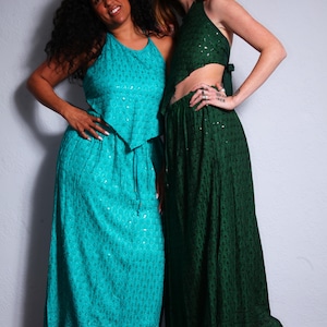 May include: Two women wearing matching turquoise and emerald green outfits. The turquoise outfit includes a halter top and a long skirt. The emerald green outfit features a halter top and a long skirt. Both outfits have a subtle pattern and are suitable for a bohemian or resort style.