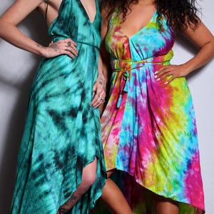 Puede incluir: Dos mujeres con vestidos teñidos con tinte anudado. Uno es verde azulado y negro, el otro una mezcla de rosa, azul y amarillo. Ambos vestidos tienen cuello halter y dobladillo asimétrico. Las mujeres están de pie sobre una alfombra estampada.