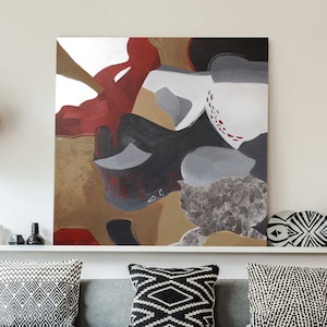 Puede incluir: Un sofá seccional gris con almohadas de tiro con patrones en blanco y negro. Una gran pintura abstracta con colores rojo, marrón, gris y blanco cuelga sobre el sofá. Una mesa de café de madera se encuentra frente al sofá.