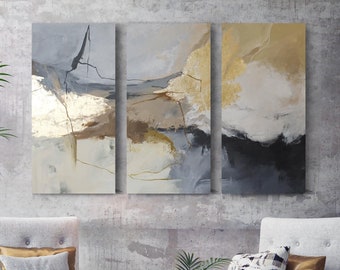 May include: Three-panel abstract art with gold and neutral tones hangs above two gray armchairs. A small round table and a patterned floor complete the modern living room setting. Decorative pillows and a small ottoman add to the decor.