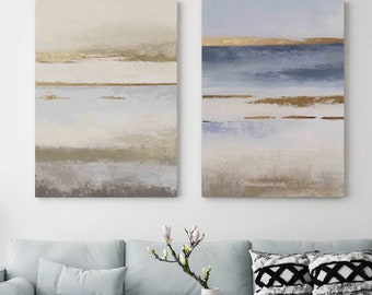 May include: Two rectangular wall art canvases featuring horizontal bands of color. The left canvas displays beige, cream, and gold tones. The right canvas features blue, white, and gold accents. Both pieces utilize textured paint strokes.