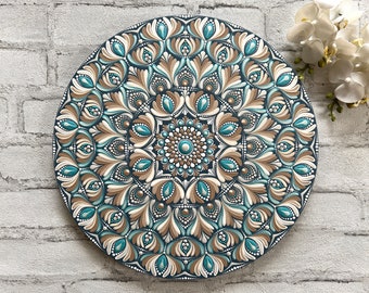 May include: A round wooden mandala painted with intricate patterns in shades of teal, brown, and white. The mandala is surrounded by a dark blue border.