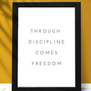 Pode incluir: Impress&atilde;o emoldurada em preto com o texto "Through discipline comes freedom" em fundo branco. A impress&atilde;o est&aacute; sobre uma superf&iacute;cie de madeira branca com uma parede amarela atr&aacute;s.