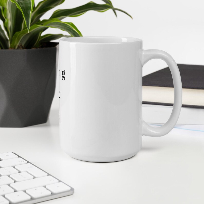 May include: White ceramic mug with a black inscription that reads "Nothing is impossible". The mug has a handle and is sitting on a white surface.