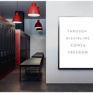 Pode incluir: Uma cita&ccedil;&atilde;o motivacional, "Through discipline comes freedom", &eacute; exibida em um p&ocirc;ster branco com moldura preta, pendurado em uma parede branca. O p&ocirc;ster est&aacute; em uma sala com arm&aacute;rios pretos e vermelhos, mesas pretas e luzes pendentes vermelhas.