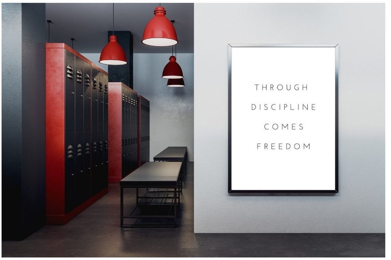 Pode incluir: Uma cita&ccedil;&atilde;o motivacional, "Through discipline comes freedom", &eacute; exibida em um p&ocirc;ster branco com moldura preta, pendurado em uma parede branca. O p&ocirc;ster est&aacute; em uma sala com arm&aacute;rios pretos e vermelhos, mesas pretas e luzes pendentes vermelhas.