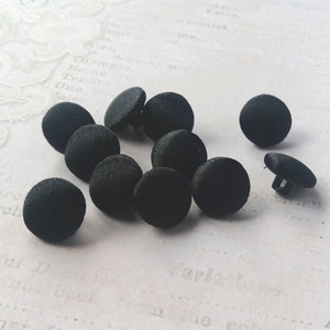 Puede incluir: Una colección de diez botones redondos negros. Los botones están hechos de una tela suave y texturizada.