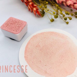 May include: A pink watercolor paint pan with gold glitter, labeled "Princesse", and a sample of the paint on a white surface.
