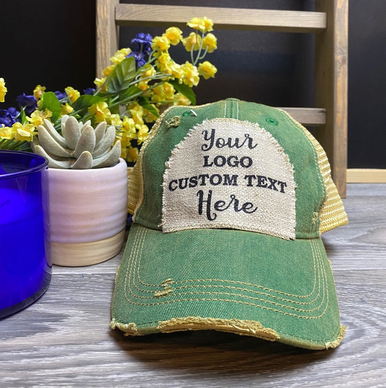 May include: Green distressed trucker hat with a beige patch that says "Your Logo Custom Text Here".