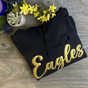 May include: Black hooded sweatshirt with a gold embroidered "Eagles" design.