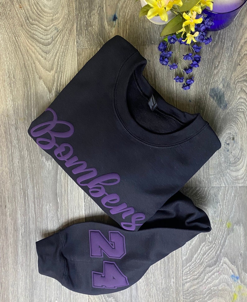 May include: Black sweatshirt with purple text that says "Bombers" and a purple number "24" on the sleeve.