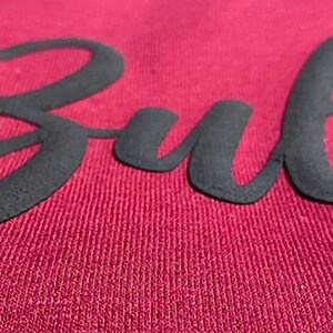 May include: Close-up of a maroon sweatshirt with the word "Bulls" in black raised lettering.