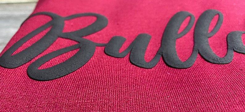 May include: Close-up of a maroon sweatshirt with the word "Bulls" in black raised lettering.