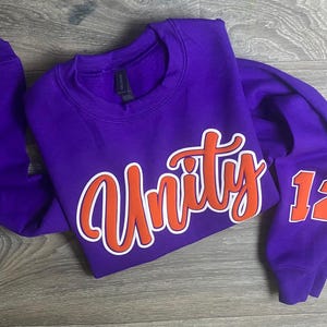 May include: Purple sweatshirt with orange and white lettering that says "Unity" and the number "12" on the sleeve.