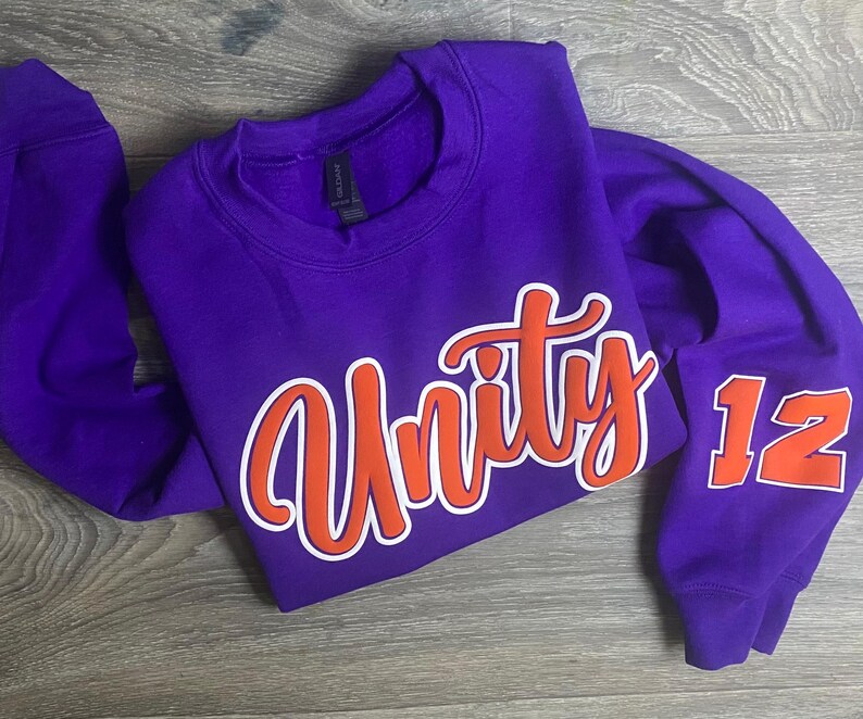 May include: Purple sweatshirt with orange and white lettering that says "Unity" and the number "12" on the sleeve.