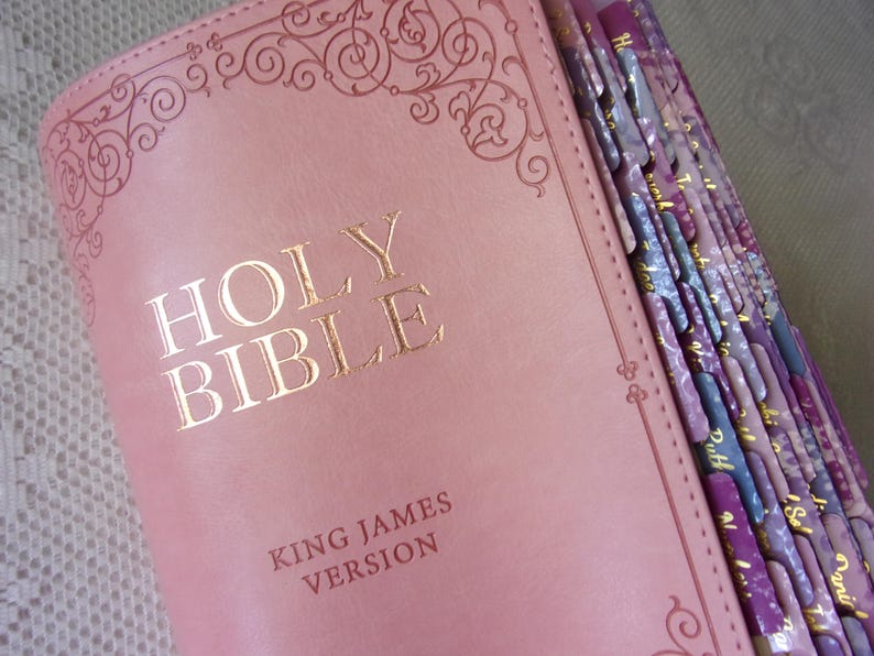 Pu&ograve; includere: Una Bibbia color rosa polvere, versione King James, con scritte in lamina d'oro sulla copertina. La copertina presenta un bordo decorativo a volute in rilievo. Il lato del libro include diverse linguette indice con motivi viola e lavanda.