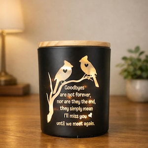 May include: Black candle holder with a wooden lid. The candle holder features a design of two birds perched on a branch, with the words "Goodbyes are not forever, nor are they the end, they simply mean I'll miss you until we meet again."
