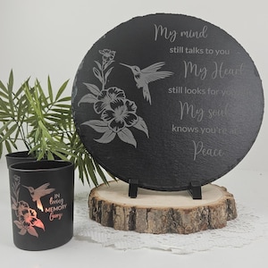 May include: A black slate memorial plaque with a hummingbird and floral design, supported by a wooden base. The plaque features the text "My mind still talks to you, My Heart still looks for you, My soul knows you're at Peace." A black candle holder with a hummingbird and floral design is also present.