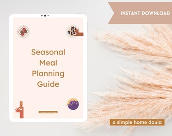 May include: A digital tablet displaying a pink background with the text "Seasonal Meal Planning Guide" in brown text. The text "a simple home doula" is also visible in brown text. The tablet is on a white surface with a beige pampas grass plant in the background.