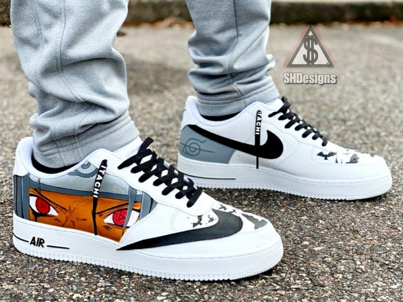 May include: White custom sneakers with a black swoosh and a black and white graphic of a character from the anime series Naruto. The character's name "ITACHI" is written on the side of the shoe.