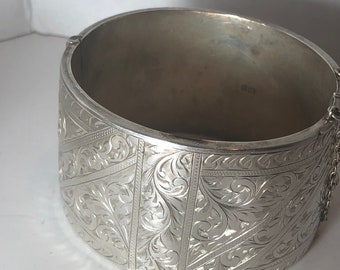 Puede incluir: Un brazalete de plata con un intrincado diseño floral. El brazalete está grabado con un patrón de hojas y vides.