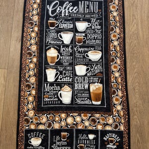 May include: A coffee-themed kitchen towel with a black chalkboard-style menu featuring various coffee drinks. The towel has a brown border with coffee cup designs and the text "Coffee" and "Happiness".