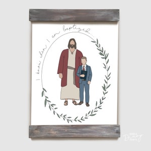 May include: A white printable art print with a hand-drawn illustration of Jesus and a young boy. The boy is holding a book and both figures are standing inside a wreath of green leaves. The text "I know when I am baptized..." is written in cursive around the wreath.