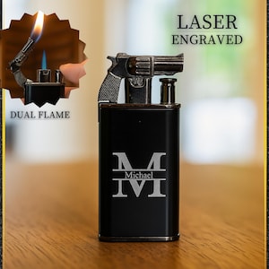 May include: Black rectangular lighter with a gun-shaped top and the text "LASER ENGRAVED". The lighter has a dual flame feature and the text "DUAL FLAME". The front of the lighter is engraved with the letter "M", the name "Michael", and the Roman numeral "IV".