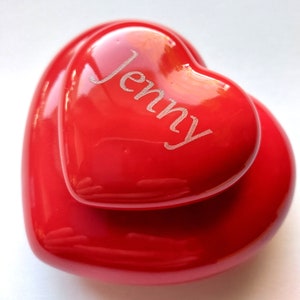 以下が含まれることがあります： 赤いハート型の箱の上に、さらに小さな赤いハート型の箱が乗っています。小さな箱には「Jenny」という名前が刻まれています。
