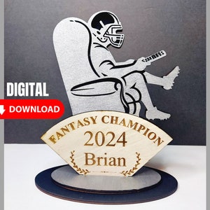 May include: A wooden trophy with a silver silhouette of a football player sitting in a chair and holding a remote control. The trophy has a wooden base with the text "Fantasy Champion 2024 Brian" engraved on it.