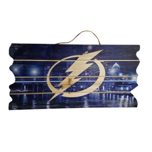 May include: A wooden sign with a blue and white cityscape and a lightning bolt logo. The sign has a distressed look and is perfect for a sports fan.