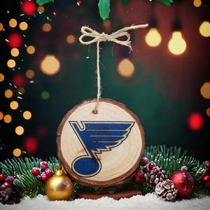 May include: A wooden Christmas bauble featuring the St. Louis Blues hockey team logo. The bauble is blue and gold and has a string attached to the top for hanging.