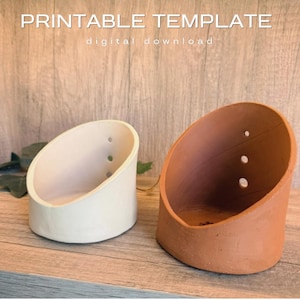 Op de afbeelding: Twee schuin afgesneden cilindrische plantenbakken, één in gebroken wit en één in terracotta, elk met drie kleine ronde drainagegaten aan de zijkant. De tekst PRINTABLE TEMPLATE digital download is zichtbaar bovenaan de afbeelding.