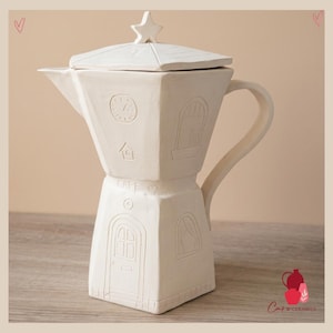 Op de afbeelding: Een witte keramische koffiepot met een stervormige knop op het deksel. De pot heeft reliëfdetails, waaronder een klok, een huis, ramen en een deur. Het woord "CAFE" is ook in reliëf aangebracht. De pot heeft een handvat en een tuit.
