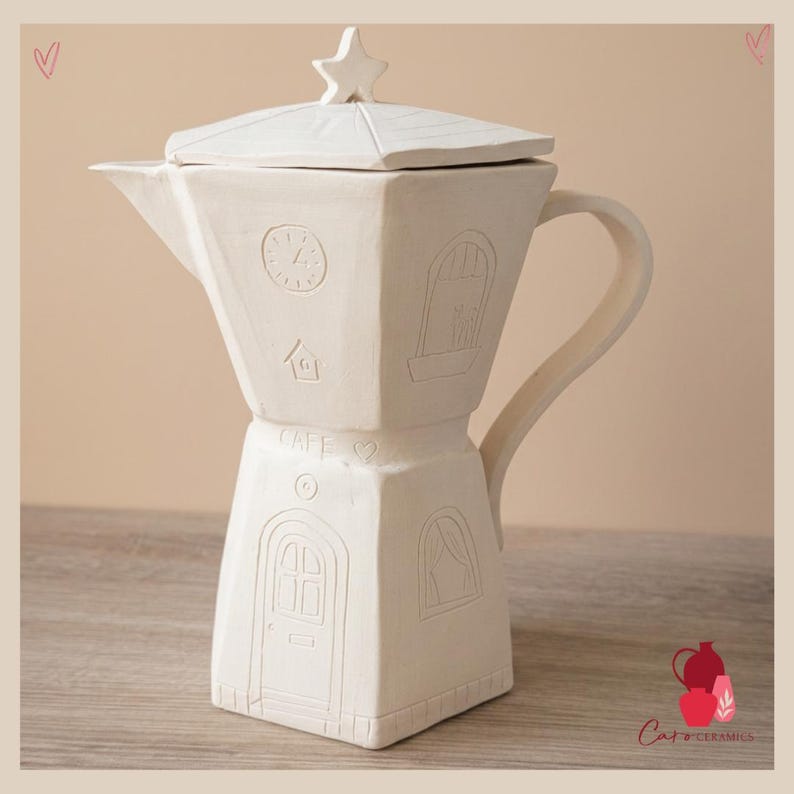 Może przedstawiać: Biały ceramiczny dzbanek do kawy z gwiazdką na pokrywce. Dzbanek posiada wytłoczone detale, w tym zegar, dom, okna i drzwi. Słowo "CAFE" jest r&oacute;wnież wytłoczone. Dzbanek ma uchwyt i dzi&oacute;bek.