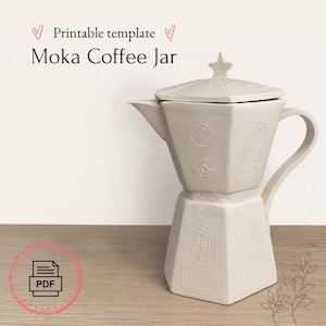 Op de afbeelding: Een lichtbeige Moka koffiepot met een stervormig deksel en een handvat. De pot heeft reliëfdetails, waaronder een klok, een huis en een deur. De tekst "Moka Coffee Jar" staat erboven.