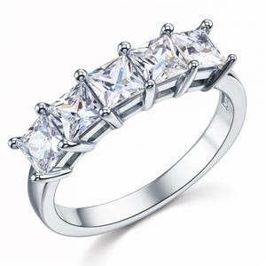May include: A silver ring with four square-shaped clear gemstones set in a row.